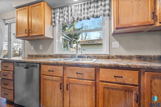 kitchen with stainless steel dishwasher, brown cabinetry, dark countertops, and a sink