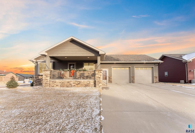 view of front of house with an attached garage, covered porch, stone siding, concrete driveway, and roof with shingles