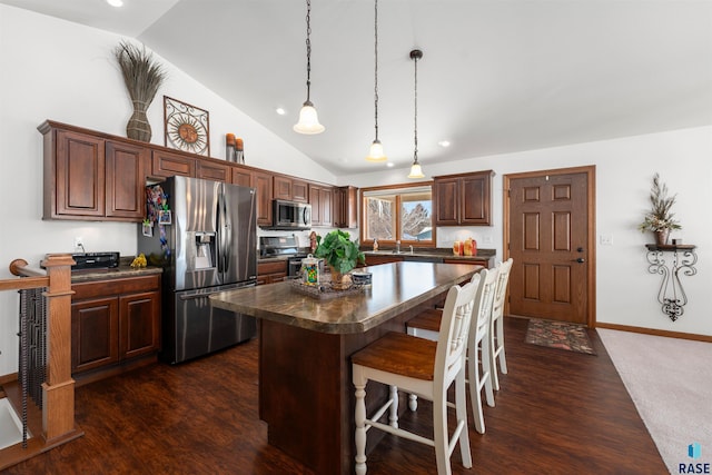 kitchen with a breakfast bar area, dark wood-type flooring, a kitchen island, appliances with stainless steel finishes, and dark countertops