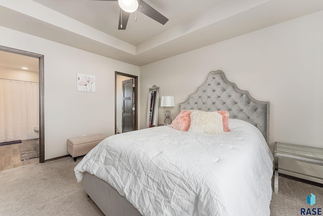 bedroom featuring carpet, a raised ceiling, a ceiling fan, ensuite bath, and baseboards