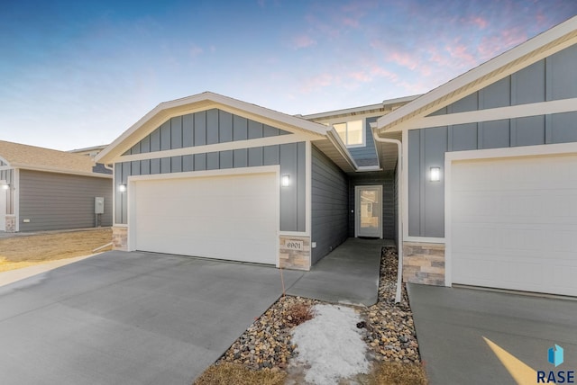 ranch-style house with driveway, stone siding, board and batten siding, and an attached garage