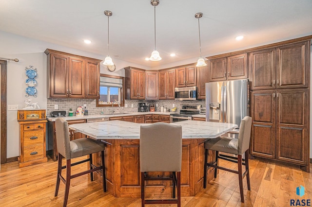 kitchen featuring tasteful backsplash, appliances with stainless steel finishes, a sink, and light wood-style floors