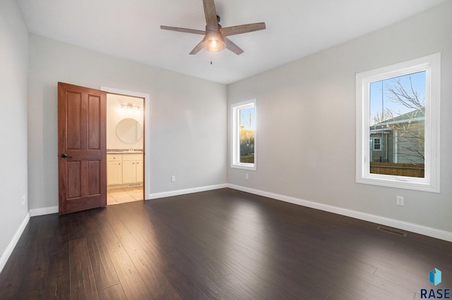 unfurnished bedroom featuring ensuite bathroom, dark wood-type flooring, visible vents, and baseboards