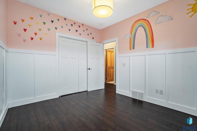 unfurnished bedroom with a wainscoted wall, dark wood-style flooring, a closet, and visible vents