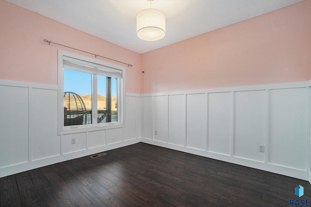 spare room with visible vents, a decorative wall, dark wood-style flooring, and wainscoting