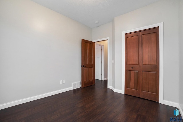 unfurnished bedroom with baseboards, a closet, visible vents, and dark wood-style flooring