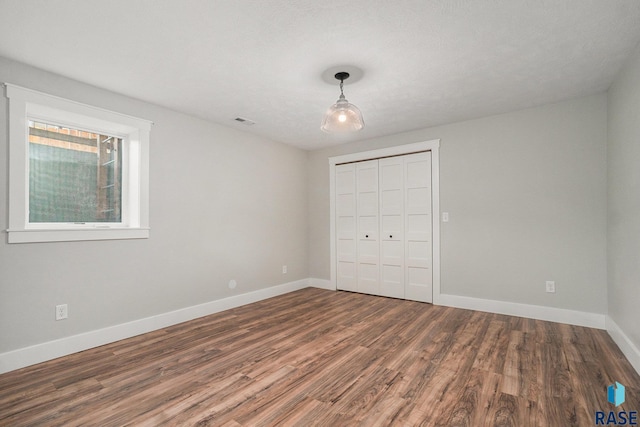 unfurnished bedroom featuring a closet, wood finished floors, visible vents, and baseboards