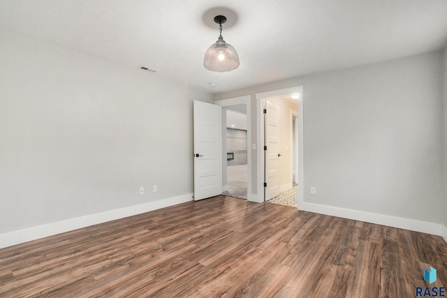 unfurnished bedroom with visible vents, connected bathroom, baseboards, and wood finished floors