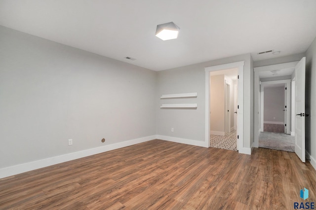 unfurnished room featuring wood finished floors, visible vents, and baseboards