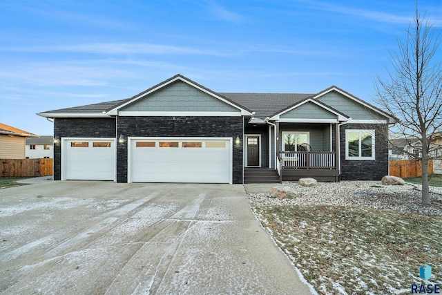 view of front of property featuring a porch, an attached garage, fence, stone siding, and driveway