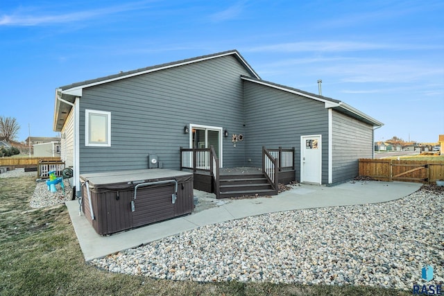 rear view of house with a deck, a patio area, fence, and a hot tub