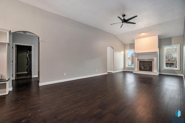 unfurnished living room featuring arched walkways, ceiling fan, dark wood-style flooring, vaulted ceiling, and a glass covered fireplace