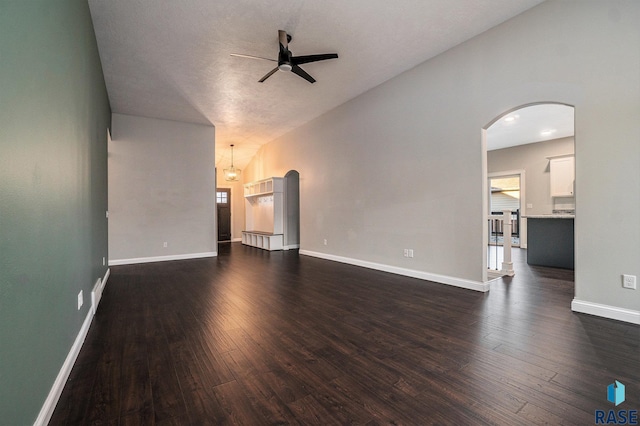 unfurnished living room featuring arched walkways, dark wood finished floors, lofted ceiling, ceiling fan, and baseboards