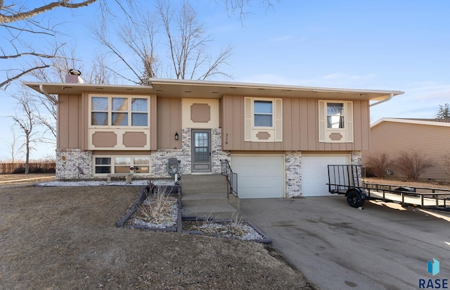 bi-level home featuring brick siding, a chimney, board and batten siding, a garage, and driveway