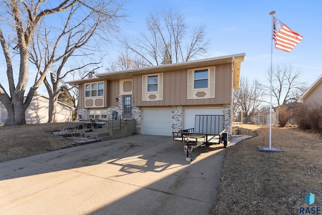 split foyer home with an attached garage, stone siding, and concrete driveway