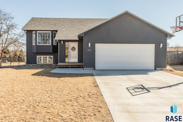 split level home with an attached garage, driveway, fence, and roof with shingles