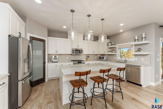 kitchen with a breakfast bar area, a sink, white cabinetry, appliances with stainless steel finishes, and open shelves