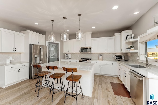 kitchen with a center island, a breakfast bar, open shelves, appliances with stainless steel finishes, and a sink