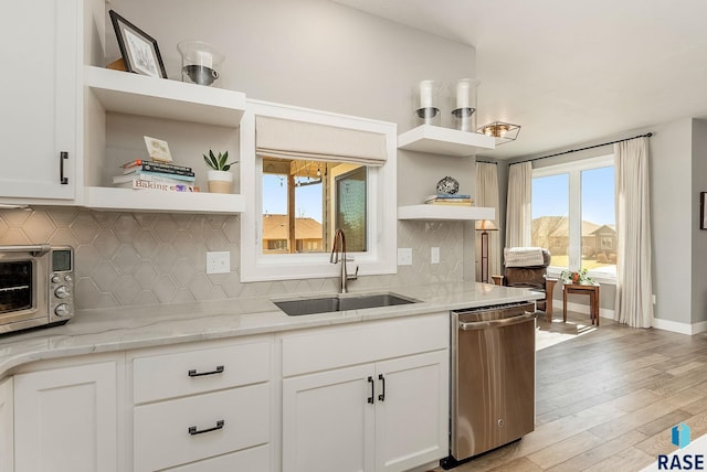 kitchen with open shelves, stainless steel dishwasher, light wood-style floors, white cabinets, and a sink