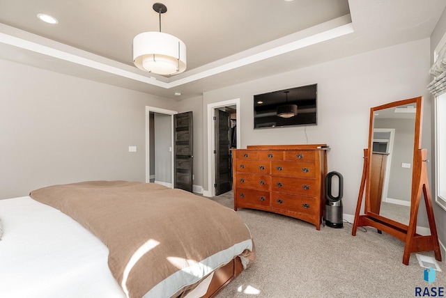 bedroom featuring a walk in closet, a raised ceiling, light carpet, and baseboards