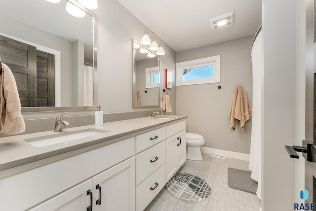 bathroom with toilet, double vanity, baseboards, and a sink