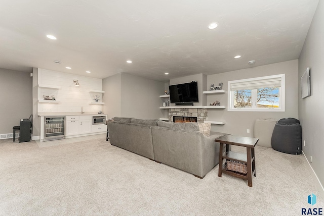 living area featuring beverage cooler, light colored carpet, a bar, a fireplace, and recessed lighting