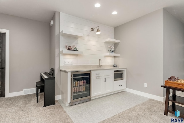 bar featuring light carpet, beverage cooler, stainless steel microwave, wet bar, and a sink