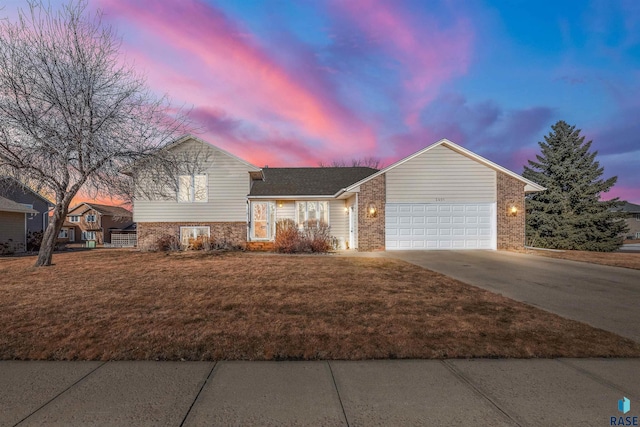 split level home featuring an attached garage, brick siding, driveway, and a front lawn