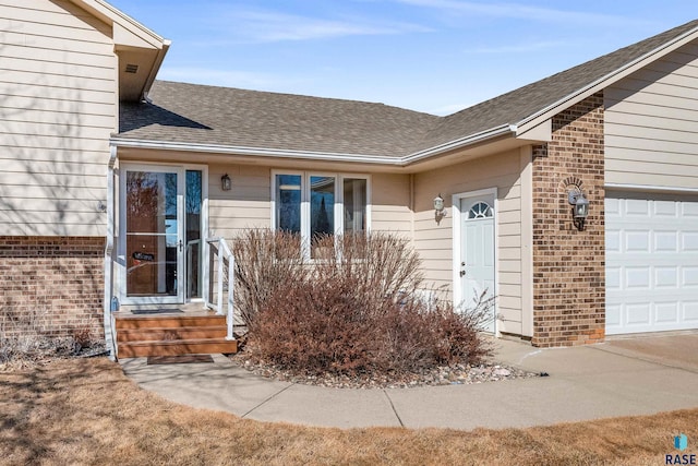 doorway to property featuring a garage, roof with shingles, and brick siding