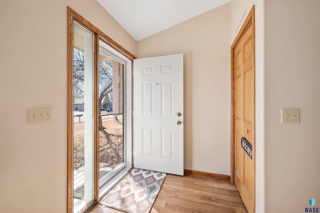 entryway with light wood-style floors, baseboards, and vaulted ceiling