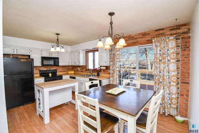 kitchen featuring butcher block countertops, a sink, light wood-style floors, black appliances, and an inviting chandelier