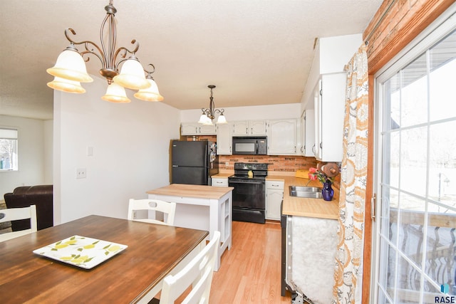 kitchen with backsplash, light wood-style floors, a sink, butcher block countertops, and black appliances