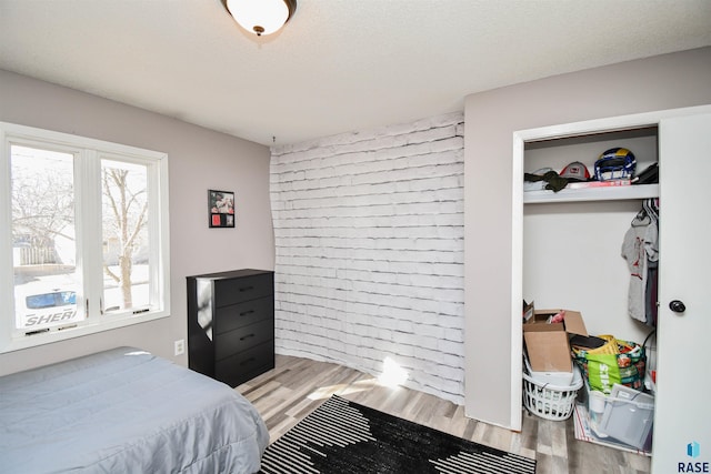 bedroom featuring brick wall, a textured ceiling, and wood finished floors