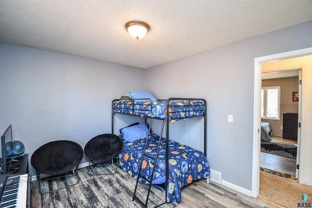 bedroom featuring visible vents, a textured ceiling, baseboards, and wood finished floors