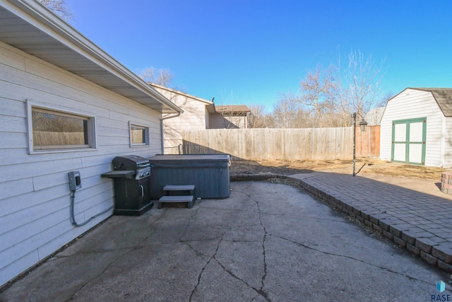 view of patio featuring fence, a hot tub, an outdoor structure, and a shed