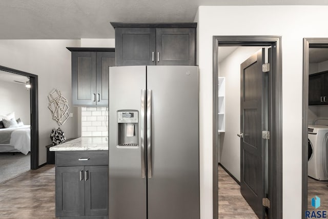 kitchen featuring washer / clothes dryer, stainless steel refrigerator with ice dispenser, decorative backsplash, and wood finished floors