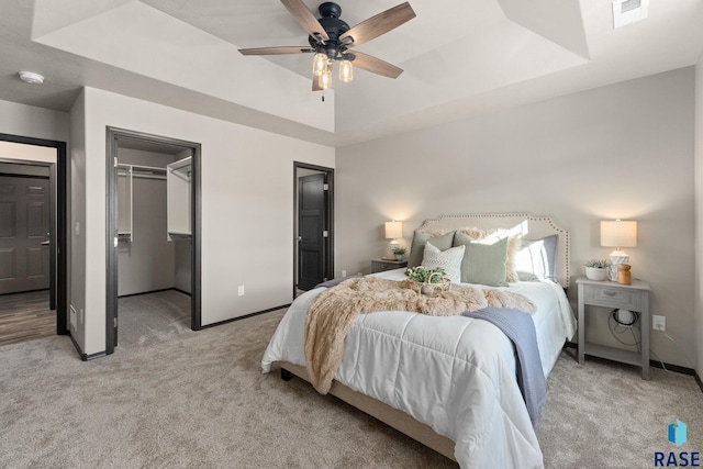 bedroom with a walk in closet, a raised ceiling, light colored carpet, and baseboards