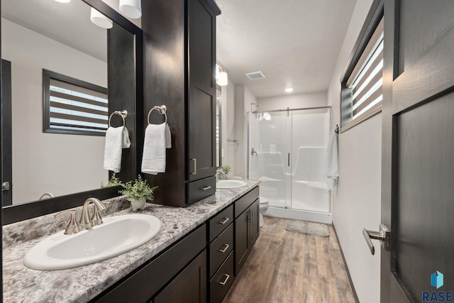 full bath featuring visible vents, a sink, a shower stall, and wood finished floors