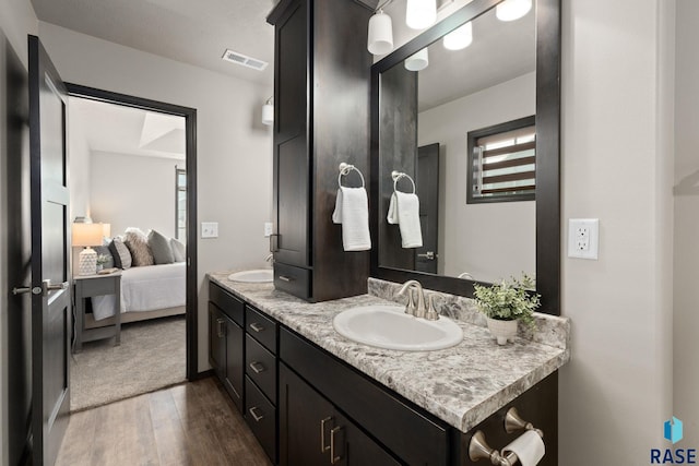 ensuite bathroom featuring double vanity, visible vents, connected bathroom, a sink, and wood finished floors