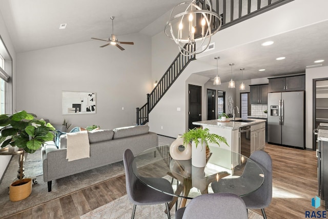 dining area featuring light wood finished floors, wine cooler, stairs, high vaulted ceiling, and ceiling fan with notable chandelier