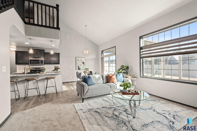 living room with high vaulted ceiling, baseboards, a chandelier, and light wood-style floors