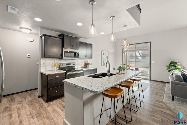 kitchen with a breakfast bar, a sink, appliances with stainless steel finishes, backsplash, and light wood finished floors