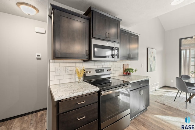 kitchen with light wood-style flooring, vaulted ceiling, appliances with stainless steel finishes, and decorative backsplash