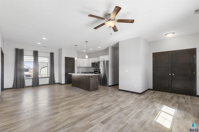 kitchen featuring open floor plan, stainless steel appliances, light wood-style flooring, and white cabinets