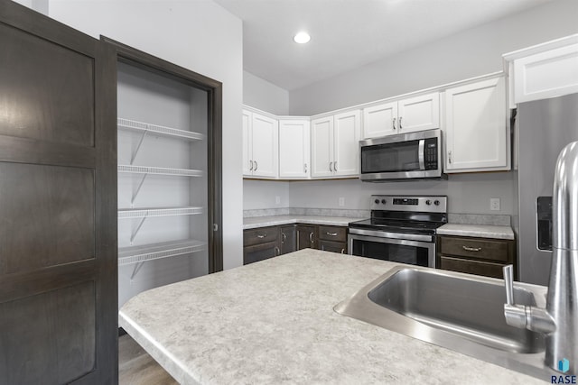 kitchen with white cabinets, stainless steel appliances, light countertops, a sink, and recessed lighting