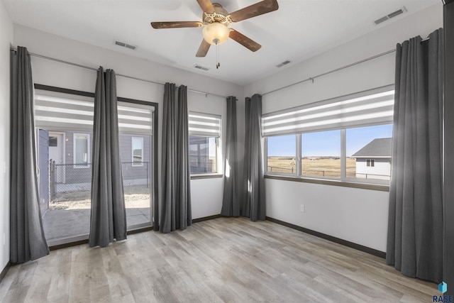 empty room with light wood-type flooring, visible vents, and baseboards