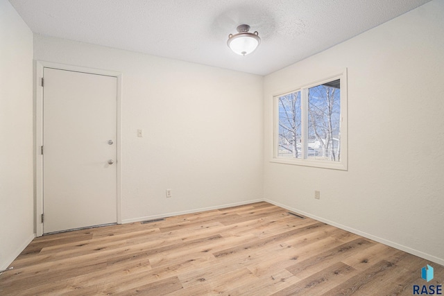 unfurnished room with visible vents, a textured ceiling, baseboards, and wood finished floors