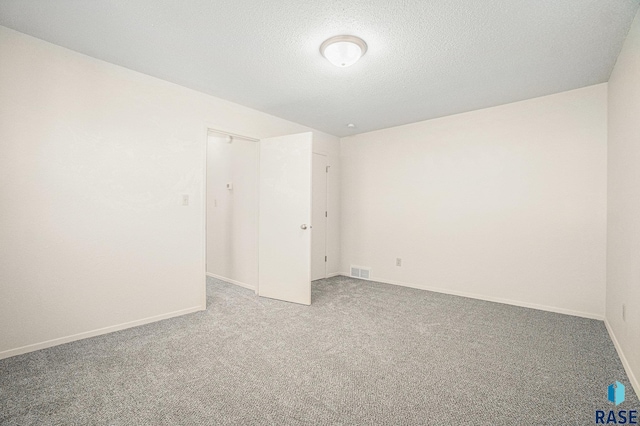 empty room featuring carpet floors, baseboards, visible vents, and a textured ceiling