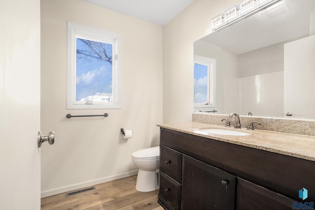 bathroom featuring visible vents, toilet, vanity, wood finished floors, and baseboards