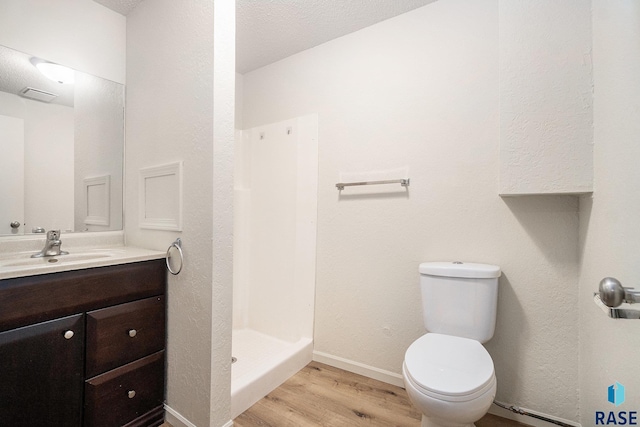 bathroom with toilet, a stall shower, vanity, wood finished floors, and baseboards